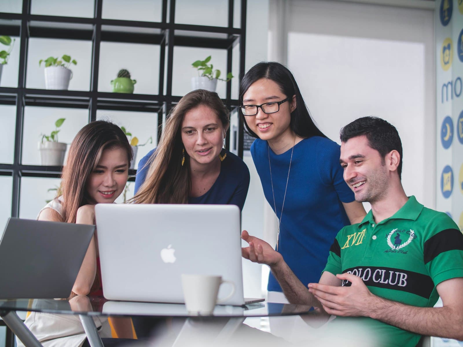 Four colleagues smiling as they look at a laptop together