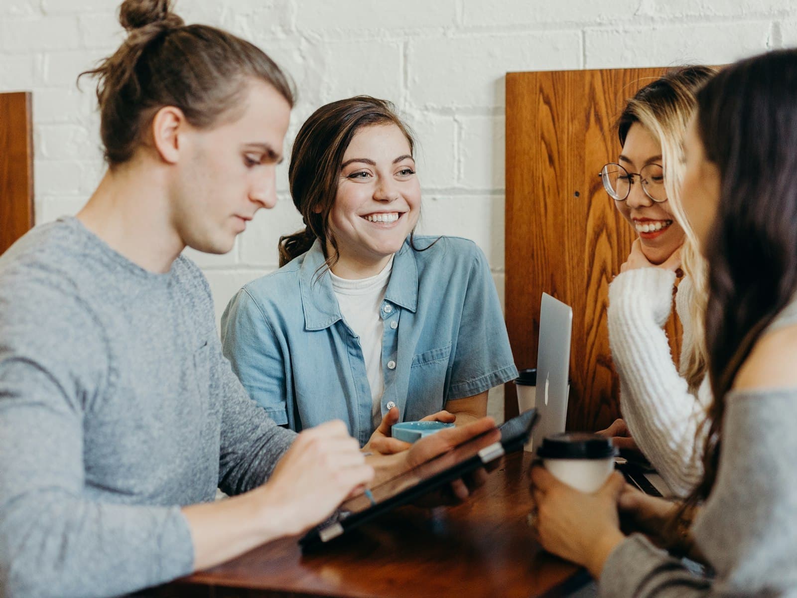 Four colleagues laughing together around a table with laptops and coffee