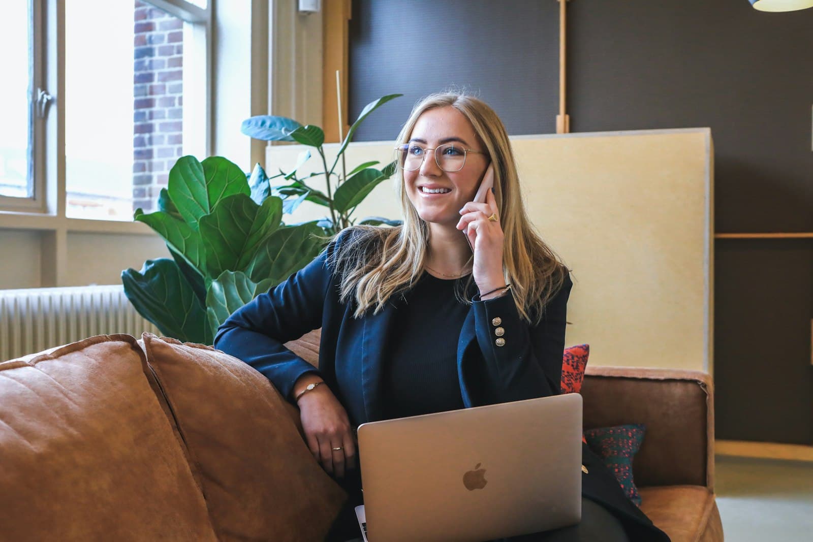 A woman laughing on a phone call with a laptop on her lap in a bright lounge