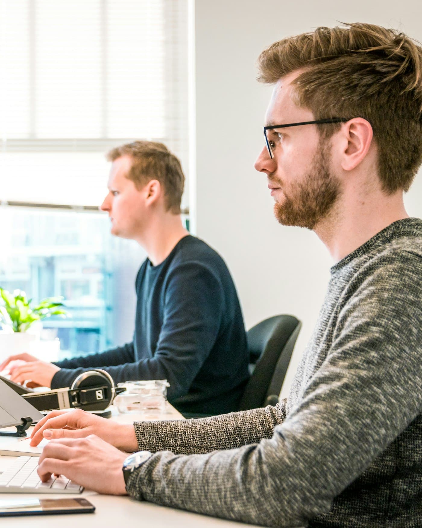 Two engineers working side by side at bright desks with laptops
