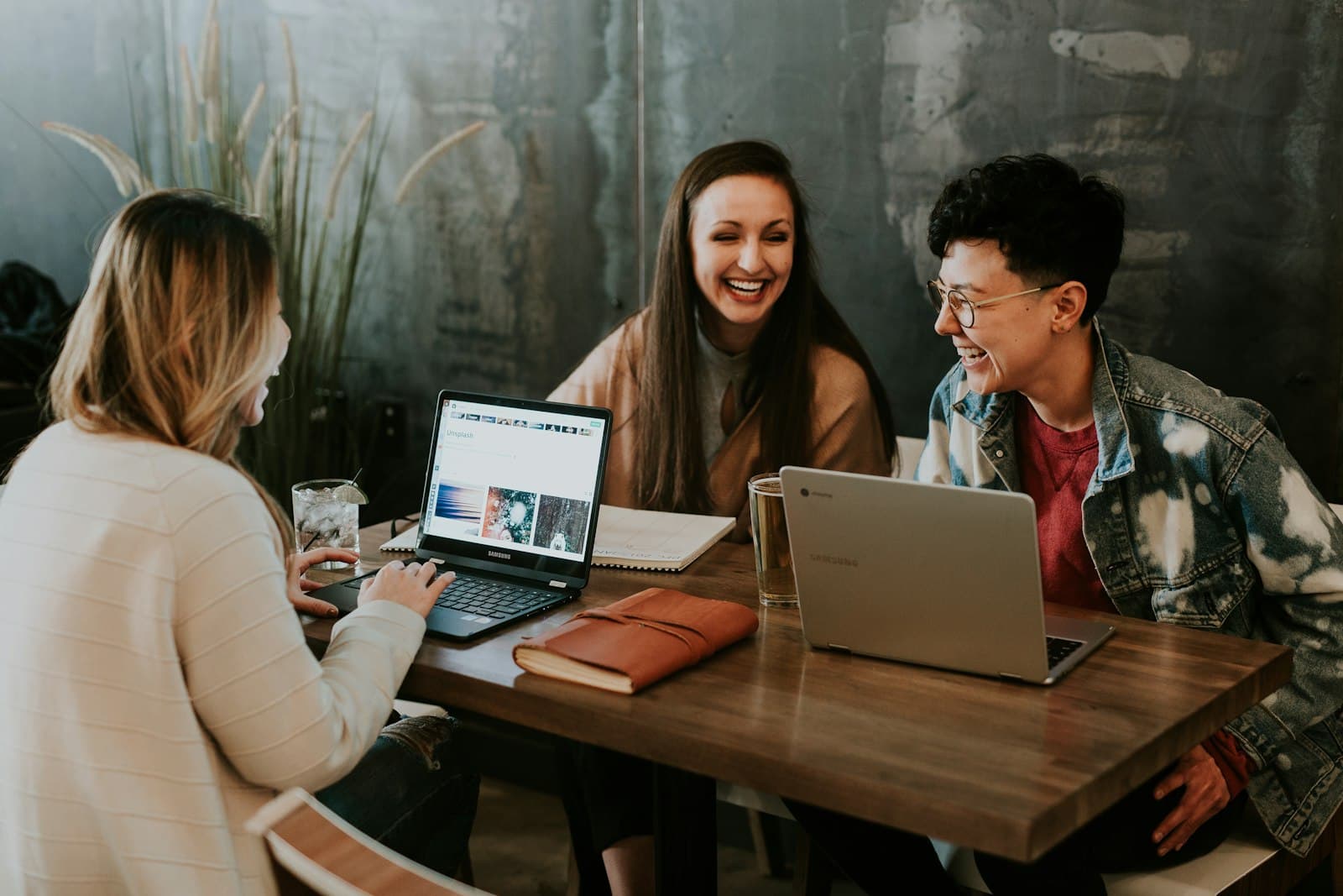 Three friends laughing together over laptops at a café table